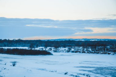 Güzel kış manzarası, bulutlu gün batımı, uzaktaki orman, kardaki tarla ve ağaçlar, dondurucu güneşli bir akşam, Ukrayna