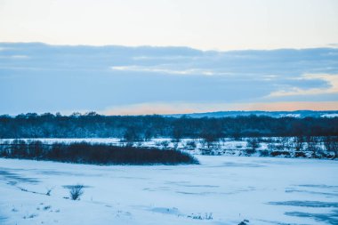 Güzel kış manzarası, bulutlu gün batımı, uzaktaki orman, kardaki tarla ve ağaçlar, dondurucu güneşli bir akşam, Ukrayna
