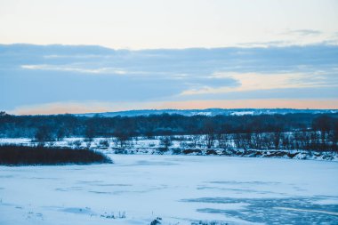 Güzel kış manzarası, bulutlu gün batımı, uzaktaki orman, kardaki tarla ve ağaçlar, dondurucu güneşli bir akşam, Ukrayna
