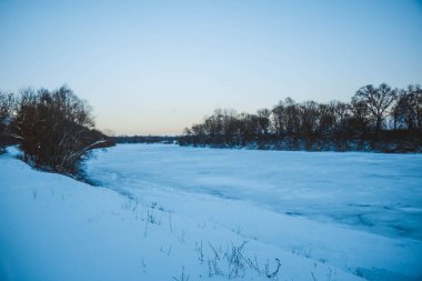 Güzel kış manzarası, bulutlu gün batımı, uzaktaki orman, kardaki tarla ve ağaçlar, dondurucu güneşli bir akşam, Ukrayna