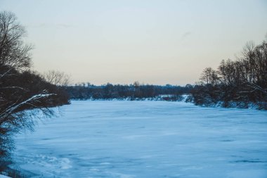 Güzel kış manzarası, bulutlu gün batımı, uzaktaki orman, kardaki tarla ve ağaçlar, dondurucu güneşli bir akşam, Ukrayna