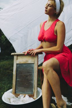 Kurutulmuş çamaşır. Genç, güzel, seksi bir kadın güneşli bir günde çamaşırlarını yıkar ve iç çamaşırlarını dışarı asar. Kırmızı elbiseli..