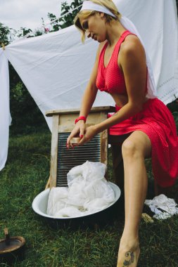 Kurutulmuş çamaşır. Genç, güzel, seksi bir kadın güneşli bir günde çamaşırlarını yıkar ve iç çamaşırlarını dışarı asar. Kırmızı elbiseli..