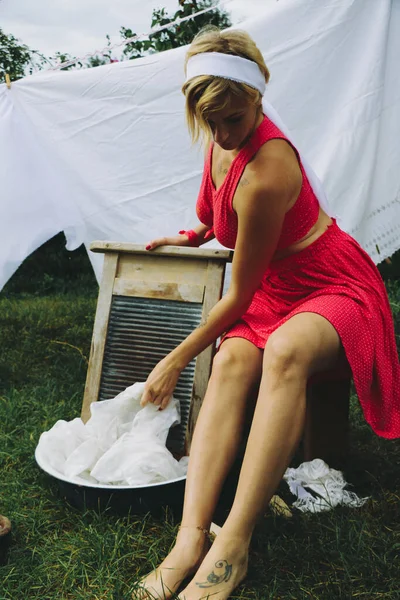 洗濯物を干した 若い美しいセクシーな女性は服を洗い 庭と晴れた日に屋外で下着を掛けます 赤い服で — ストック写真
