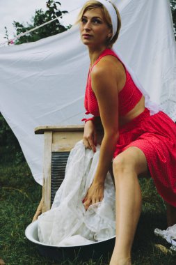 Kurutulmuş çamaşır. Genç, güzel, seksi bir kadın güneşli bir günde çamaşırlarını yıkar ve iç çamaşırlarını dışarı asar. Kırmızı elbiseli..