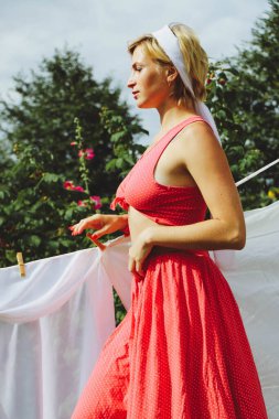 Kurutulmuş çamaşır. Genç, güzel, seksi bir kadın güneşli bir günde çamaşırlarını yıkar ve iç çamaşırlarını dışarı asar. Kırmızı elbiseli..