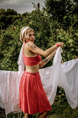 Kurutulmuş çamaşır. Genç, güzel, seksi bir kadın güneşli bir günde çamaşırlarını yıkar ve iç çamaşırlarını dışarı asar. Kırmızı elbiseli..
