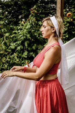 Kurutulmuş çamaşır. Genç, güzel, seksi bir kadın güneşli bir günde çamaşırlarını yıkar ve iç çamaşırlarını dışarı asar. Kırmızı elbiseli..