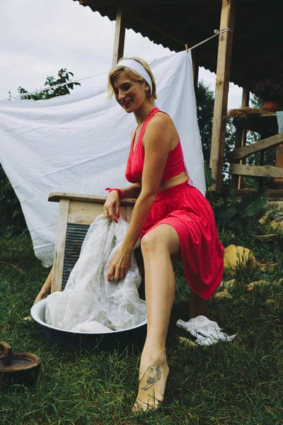 洗濯物を干した 若い美しいセクシーな女性は服を洗い 庭と晴れた日に屋外で下着を掛けます 赤い服で — ストック写真