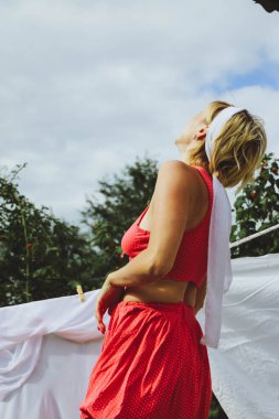 Kurutulmuş çamaşır. Genç, güzel, seksi bir kadın güneşli bir günde çamaşırlarını yıkar ve iç çamaşırlarını dışarı asar. Kırmızı bluzlu ve beyaz külotlu