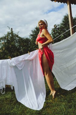 Kurutulmuş çamaşır. Genç, güzel, seksi bir kadın güneşli bir günde çamaşırlarını yıkar ve iç çamaşırlarını dışarı asar. Kırmızı bluzlu ve beyaz külotlu