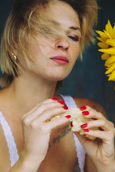 一个有趣的金发性感女人的画像 她一头金发 在一座老房子的门廊边的桌子边吃饭 一束向日葵 — 图库照片