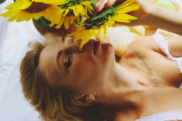 Portre Güzel genç seksi kadın, kısa sarı saçlı, Avrupalı, güneşli bir günde açık havada şehvetli bir ayçiçeği koklar. Yakın plan, yukarıdan.