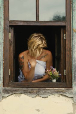 Güzel bir genç kadının sanat portresi, eski bir pencereden dışarı bakar, pencere eşiğinde grunge stiliyle oturur..