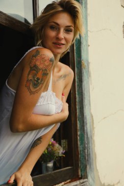 Güzel bir genç kadının sanat portresi, eski bir pencereden dışarı bakar, pencere eşiğinde grunge stiliyle oturur..