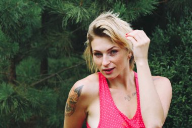 Genç, güzel, mutlu, Avrupalı sarışın kadın portresi. Yeşil bahçe arka planında iyi eğlenceler. Kırmızı elbiseli kadın eski moda raptiye stili.