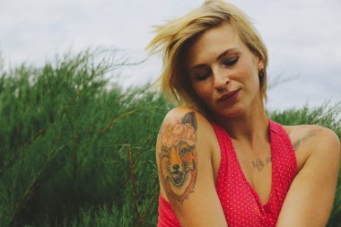 Genç, güzel, mutlu, Avrupalı sarışın kadın portresi. Yeşil bahçe arka planında iyi eğlenceler. Kırmızı elbiseli kadın eski moda raptiye stili.