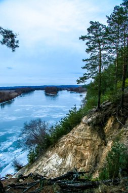Buz ve karla kaplı donmuş nehir, üst manzara. Çam ağaçlı Sandy Hill. Kış ormanı ve nehir, karlı doğa. Kış dondurucu soğuk. güzel buz dokusu
