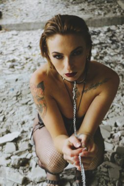 Güzel bir genç kadın, parlak makyajlı, siyah bir korse içinde, tasmalı, boyun eğen, şefkat gösteren bir tasmayla, özgürlüğün kısıtlanmasını, kadınların şiddetini gösteriyor. Harabelerde bir yerde.