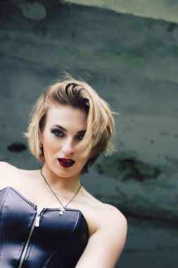 Güzel, genç bir kadın, parlak makyajlı, siyah korseli ve taytlı sarışın, seksi, grunge stili, dramatik, harap olmuş bir yerde penceresi olan.