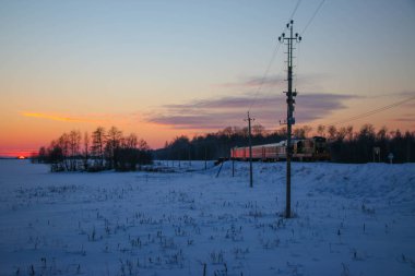 Eski bir yolcu treni soğuk bir kış akşamı gün batımında istasyona varır. Karlı manzara, güzel renkli gökyüzü.