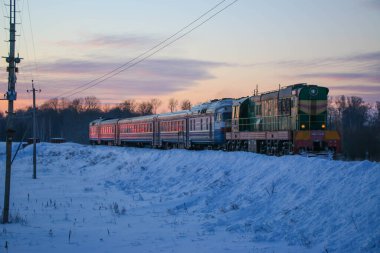 Eski bir yolcu treni soğuk bir kış akşamı gün batımında istasyona varır. Karlı manzara, güzel renkli gökyüzü.