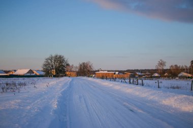 Güzel kış manzarası ağaçların arasındaki beyaz yol, mavi gökyüzü bulutlu güneşli gün, hepsi karda, ılık günbatımı ışığı