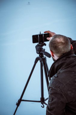 Telefonlu bir adam Zidio 'nun kış günbatımının hızlandırılmış fotoğraflarını çekiyor. Tarla, yol ve ağaçlar karla kaplı..