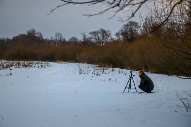 Telefonlu bir adam Zidio 'nun kış günbatımının hızlandırılmış fotoğraflarını çekiyor. Tarla, yol ve ağaçlar karla kaplı..