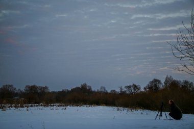 Telefonlu bir adam Zidio 'nun kış günbatımının hızlandırılmış fotoğraflarını çekiyor. Tarla, yol ve ağaçlar karla kaplı..