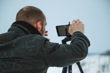 Telefonlu bir adam Zidio 'nun kış günbatımının hızlandırılmış fotoğraflarını çekiyor. Tarla, yol ve ağaçlar karla kaplı..