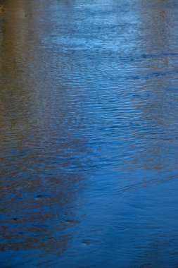 Dalgalı su yüzeyinde yansıtılan ağaçların arka planı. Kışın küçük bir nehir, karla kaplı kıyıların yansıması ve güneş parlaması. Doğal doku ve doğal renk