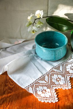 Mocap eski ahşap tahta ve mavi tabak beyaz keten masa örtüsü ve dantel havlu beyaz orkide çiçeği, güneş ışığı doğal ışık, gölge. Mutfak masası. Hoş retro, rustik arkaplan, boş alan.