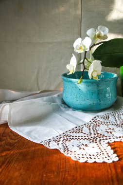 Mocap eski ahşap tahta ve mavi tabak beyaz keten masa örtüsü ve dantel havlu beyaz orkide çiçeği, güneş ışığı doğal ışık, gölge. Mutfak masası. Hoş retro, rustik arkaplan, boş alan.