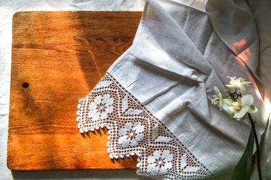 Beyaz keten masa örtüsü ve dantel havlu, beyaz orkide çiçeği, güneşli doğal ışık, gölge. Mutfak masası. Hoş retro, rustik arkaplan, boş alan.