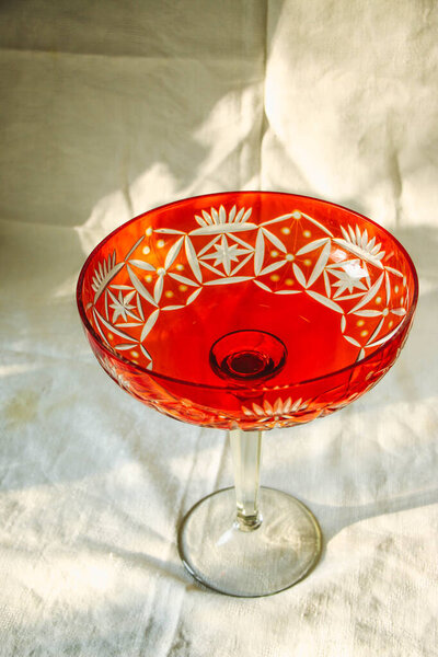 Romantic linen tea towels with cotton lace details and a red glass vintage plate with tall legs for an elegant home or restaurant service. Beautiful background, natural sunlight mockup, shadows