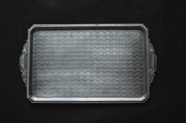 Eski dikdörtgen metal tepsi ve antika gümüş çatal bıçak takımı. Siyah arka planda, güneş ışığı, gölge. Mutfak masası, masa manzarası. Hoş retro, rustik arkaplan, boş alan.