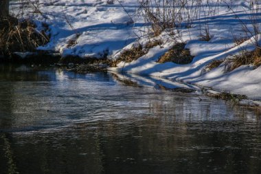 Kışın küçük bir nehir, güneşin ışınları ağaçların arasından geçer. Karlı kıyılar suya yansıyor. Kış manzarası. Kış Masalı. Kış arkaplanı.