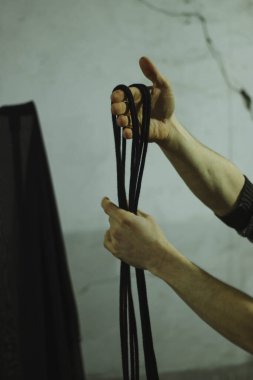 Bir adam elinde siyah Shibari ipleri, rüzgarlar ve kravatlar tutuyor. Eski gri bir duvarın arka planında dikey fotoğraf