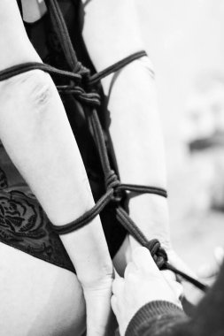 Güven Köprüsü, Shibari Dragonfly, geleneksel bir Japon şibarisine sarılı bir kadın, bir iple bağlanmış, Kinbaku. Bağlanma sürecinin siyah beyaz fotoğrafı, erkek eli.