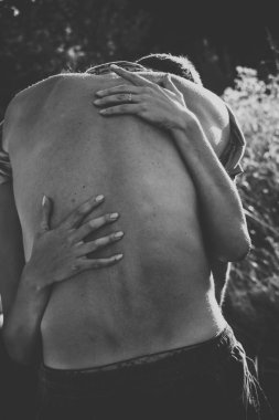 Sırtında kadın elleri olan çıplak genç bir adam. Siyah beyaz fotoğraf. Kadın nazikçe erkeği kucaklıyor. Samimiyet aşkı romantizm