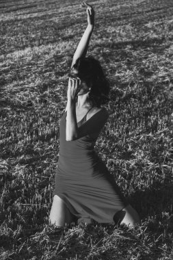 Yazın açık havada, gün batımında, biçilmiş buğday tarlasının arka planında, elbisenin içinde genç ve güzel bir esmerin portresi. Mutlu dans eden kadın, siyah beyaz fotoğraf