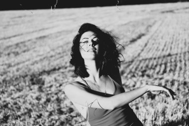 Yazın açık havada, gün batımında, biçilmiş buğday tarlasının arka planında, elbisenin içinde genç ve güzel bir esmerin portresi. Mutlu dans eden kadın, siyah beyaz fotoğraf