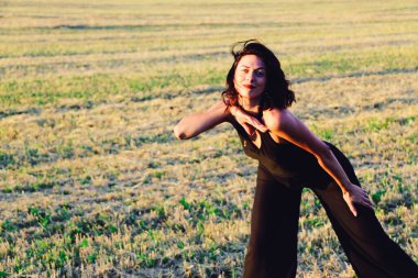 Güneşli bir yaz akşamında, gün batımında, siyah elbiseli genç ve güzel bir esmer. Çekici bir kadın dans ediyor, arka planda biçilmiş buğday gibi poz veriyor..