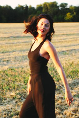 Güneşli bir yaz akşamında, gün batımında, siyah elbiseli genç ve güzel bir esmer. Çekici bir kadın dans ediyor, arka planda biçilmiş buğday gibi poz veriyor..