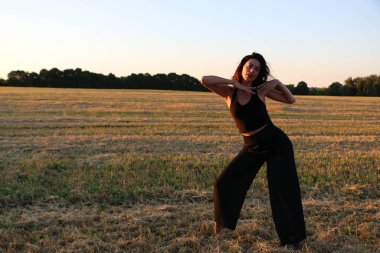 Güneşli bir yaz akşamında, gün batımında, siyah elbiseli genç ve güzel bir esmer. Çekici bir kadın dans ediyor, arka planda biçilmiş buğday gibi poz veriyor..