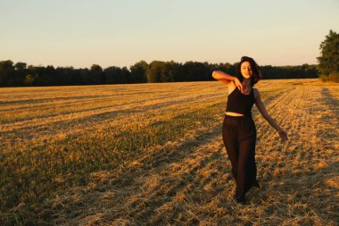 Güneşli bir yaz akşamında, gün batımında, siyah elbiseli genç ve güzel bir esmer. Çekici bir kadın dans ediyor, arka planda biçilmiş buğday gibi poz veriyor..