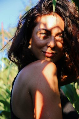 Yazın mısır yaprakları içinde güzel esmer bir kız, doğadaki bir kadının sanat portresi. Kameraya bakarak kahkahalar atmak, seçici keskinlik, açık iş gölgesi doğal ışık.