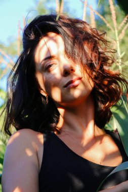 Yazın mısır yaprakları içinde güzel esmer bir kız, doğadaki bir kadının sanat portresi. Kameraya bakarak kahkahalar atmak, seçici keskinlik, açık iş gölgesi doğal ışık.