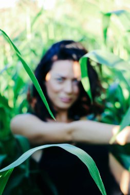 Yazın mısır yaprakları içinde güzel esmer bir kız, doğadaki bir kadının sanat portresi. Kameraya bakarak kahkahalar atmak, seçici keskinlik, açık iş gölgesi doğal ışık.
